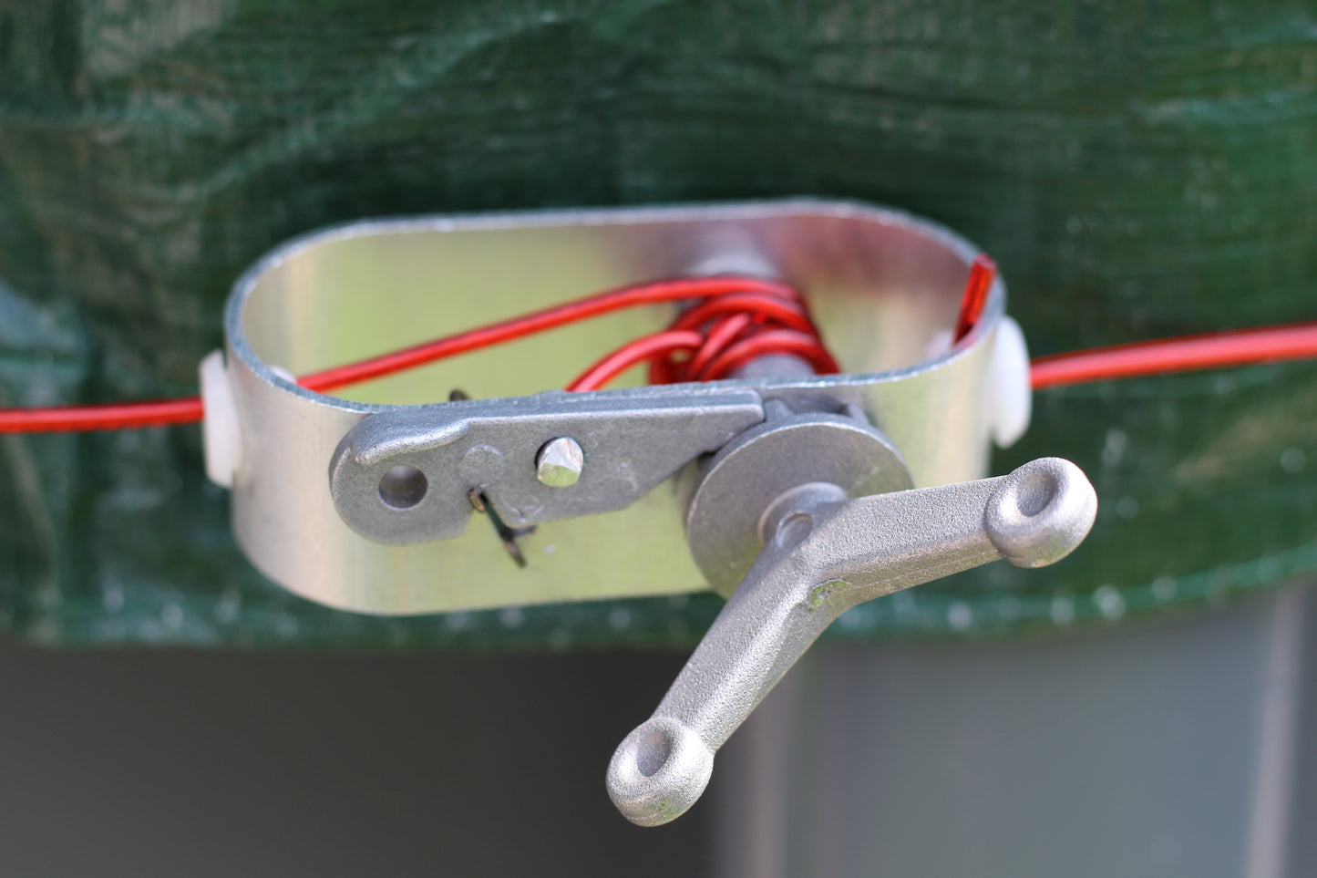 Nahaufnahme eines Metalldrahtspanners mit Griff, der einen roten Elektrozaundraht spannt - ideal zur Sicherung der HC Garten & Freizeit Sommer- & Winter-Abdeckplane für runde Pools 5,0 m.