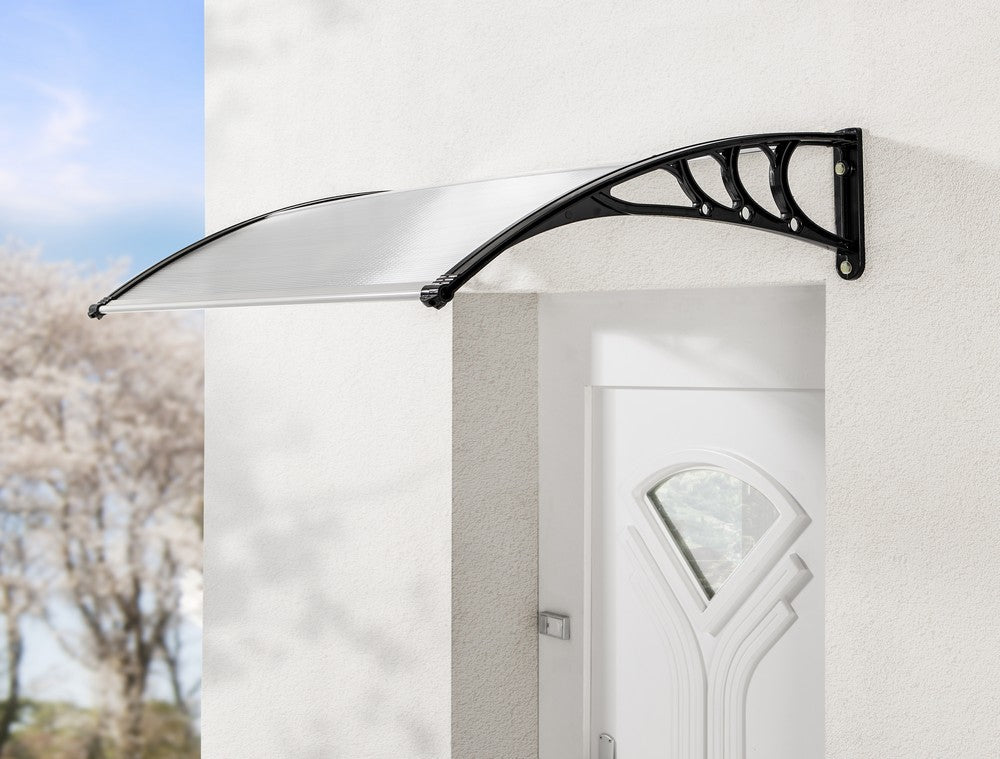 Die HC Home & Living Haustür Design-Vordach mit schwarzen Halterungen ist über einer weißen Außentür an einer hellen Wand angebracht, mit verschwommenen Bäumen und blauem Himmel im Hintergrund.