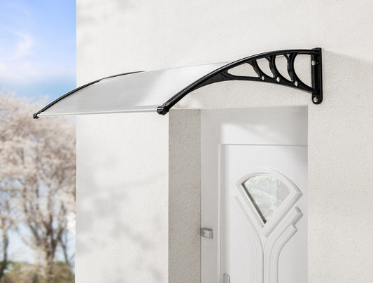 Die HC Home & Living Haustür Design-Vordach mit schwarzen Halterungen ist über einer weißen Außentür an einer hellen Wand angebracht, mit verschwommenen Bäumen und blauem Himmel im Hintergrund.