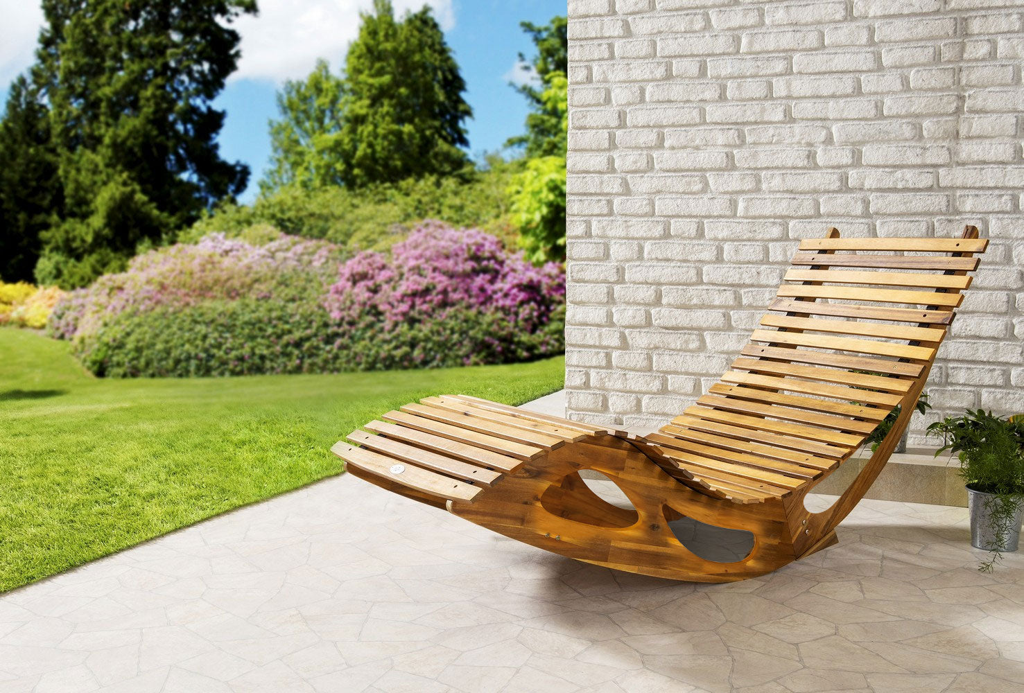 Die ergonomische Schwungliege Saunaliege aus Akazienholz von HC Garten & Freizeit - FSC® zertifiziert - steht auf der Terrasse neben einer weißen Mauer und bietet nachhaltigen Komfort mit Blick auf Rasen und blühende Büsche.