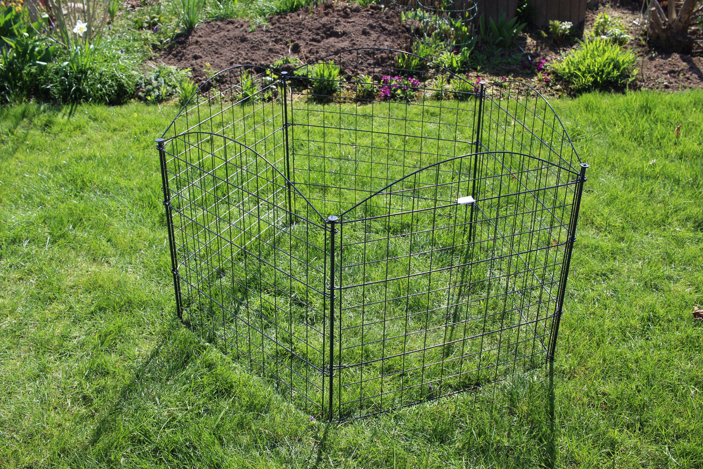 Das HC Garten & Freizeit Teichzaun Oberbogen Komplettset anthrazit von HC Garten & Freizeit, ein kompakter anthrazitfarbener Maschendrahtzaun, steht auf einer Rasenfläche inmitten üppiger Pflanzen und wirkt wie ein kleiner Gartenzaun inmitten des üppigen Grüns.