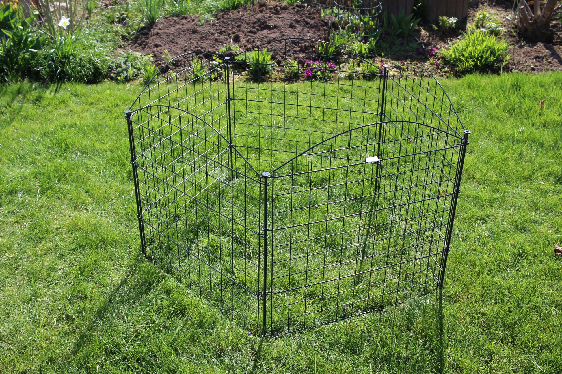 Das HC Garten & Freizeit Teichzaun Oberbogen Komplettset anthrazit von HC Garten & Freizeit, ein kompakter anthrazitfarbener Maschendrahtzaun, steht auf einer Rasenfläche inmitten üppiger Pflanzen und wirkt wie ein kleiner Gartenzaun inmitten des üppigen Grüns.
